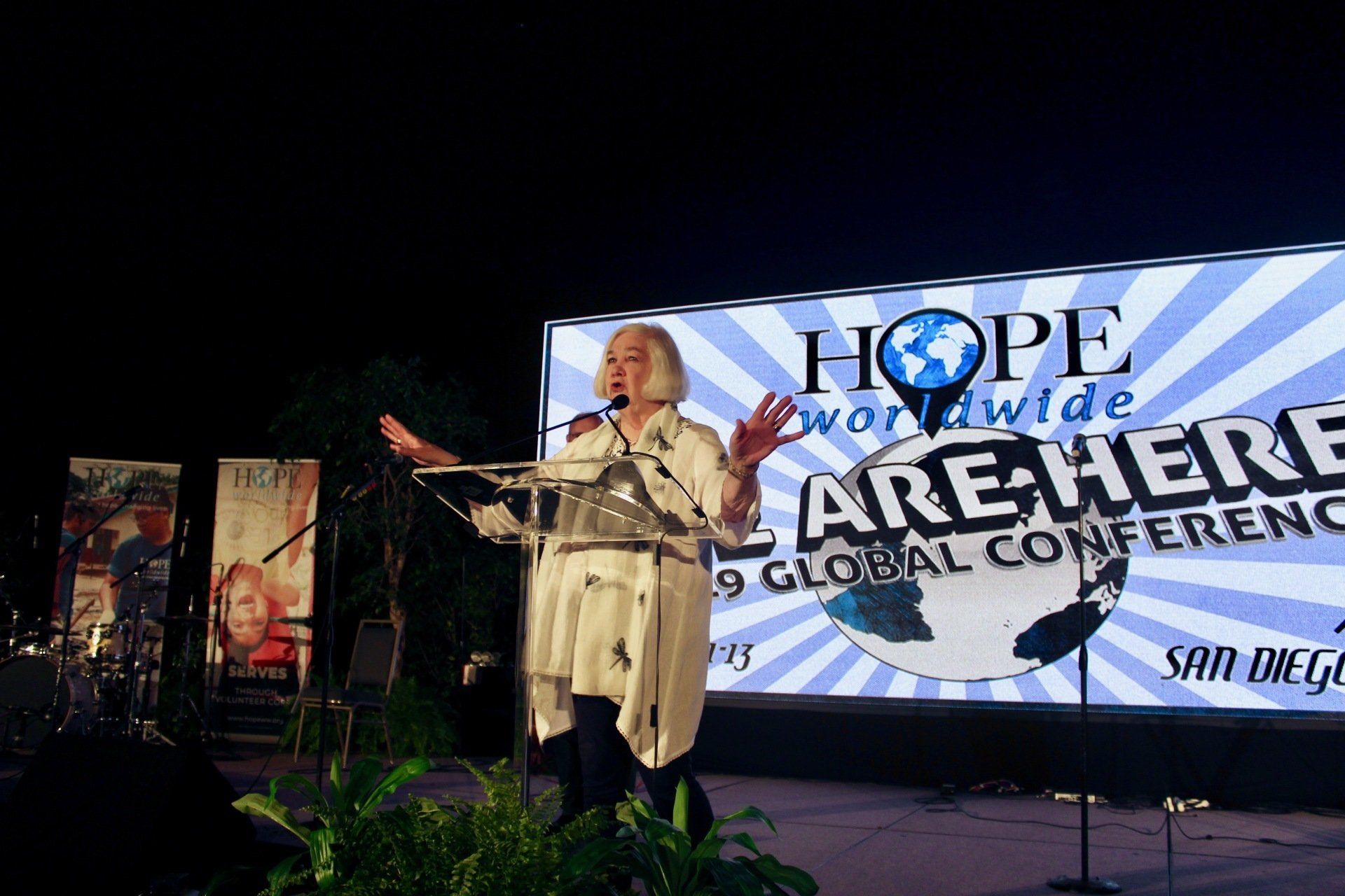 Speaker at podium on stage with large “HOPE for the World” conference banner behind her