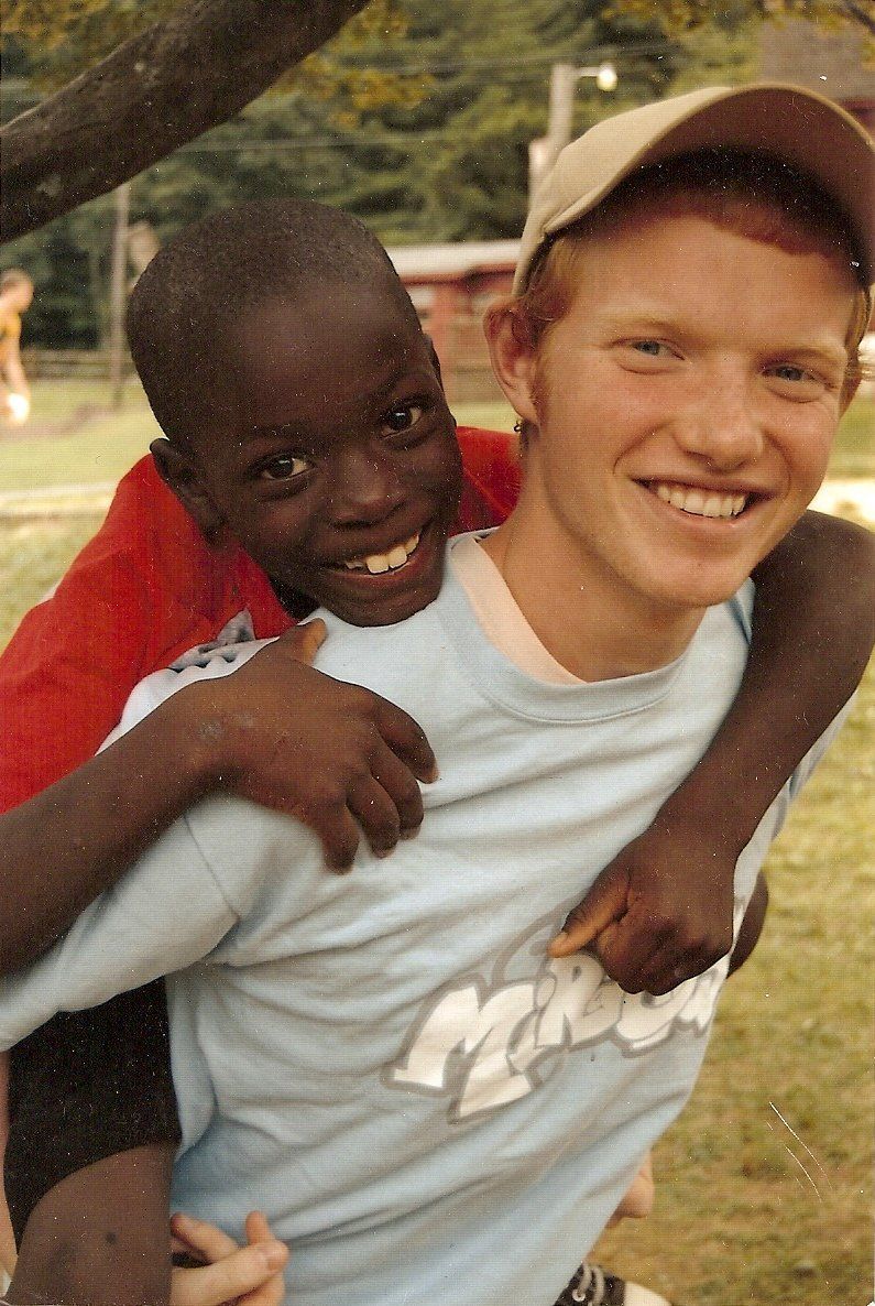 Two smiling children outdoors, one giving the other a piggyback ride.