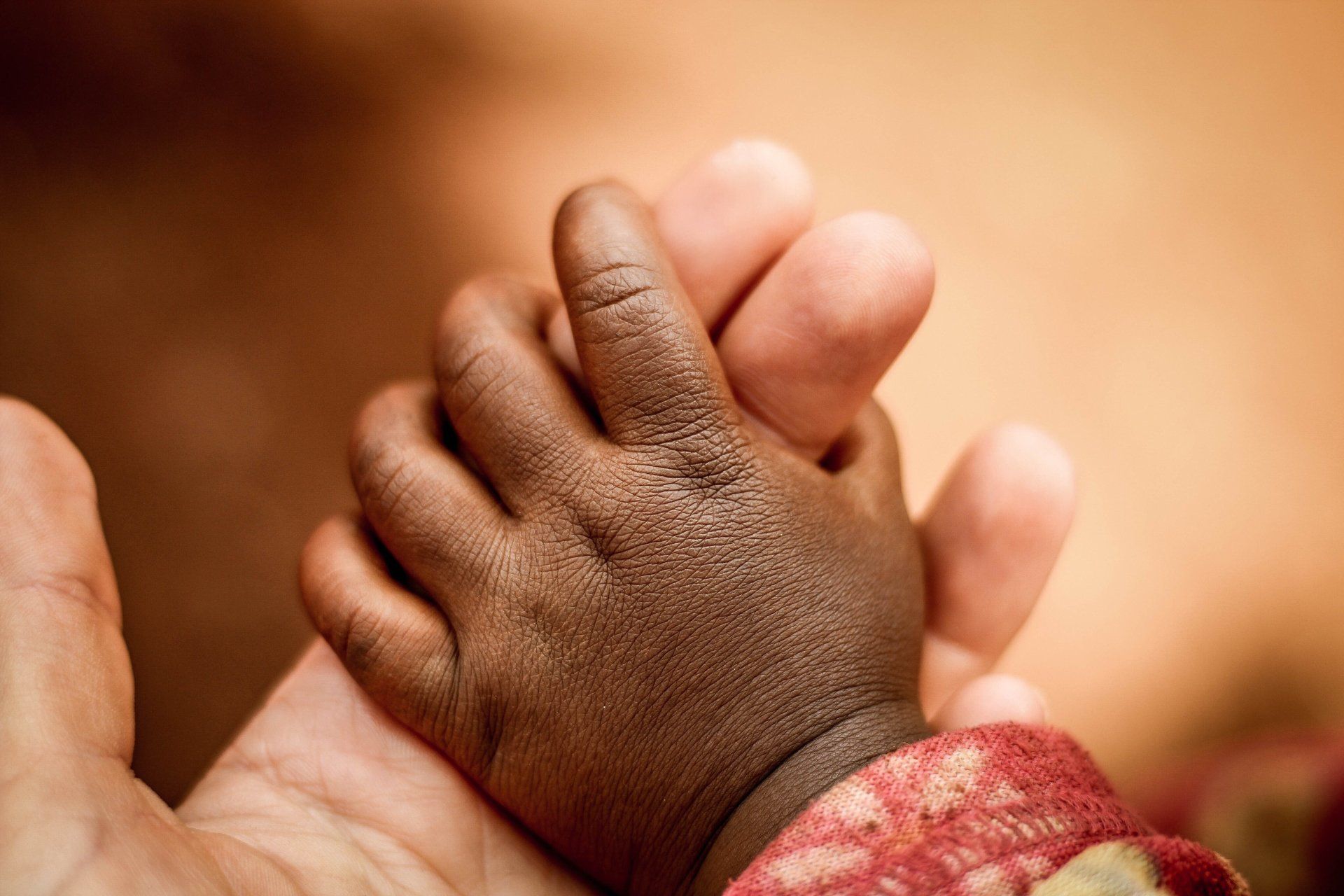 Adult hand holding a small child’s hand, close-up with warm, soft lighting