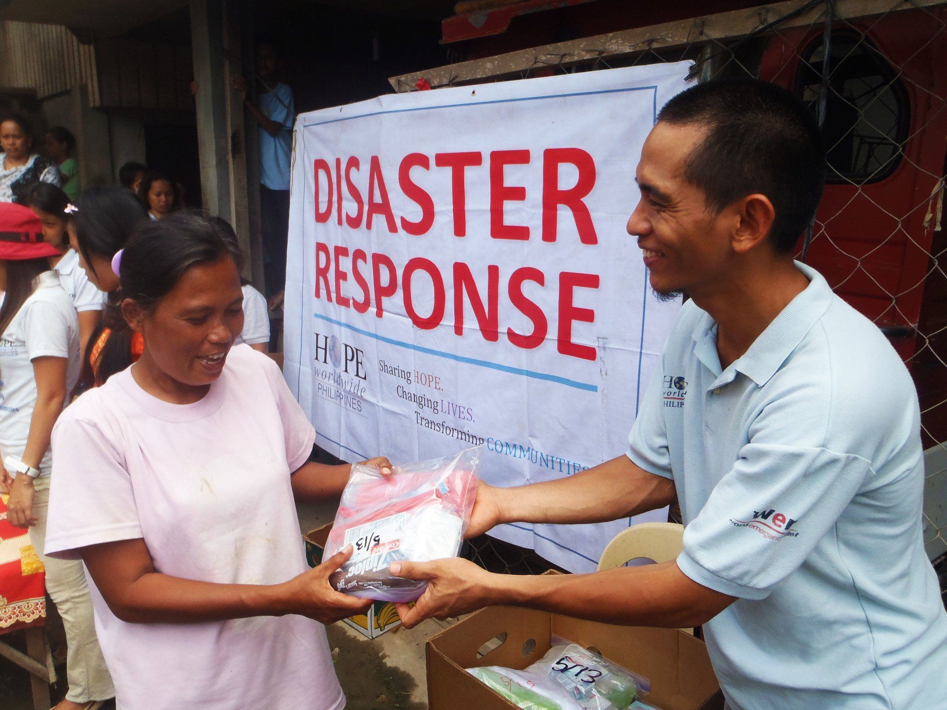 Disaster response aid being handed to a woman in front of a banner sign.