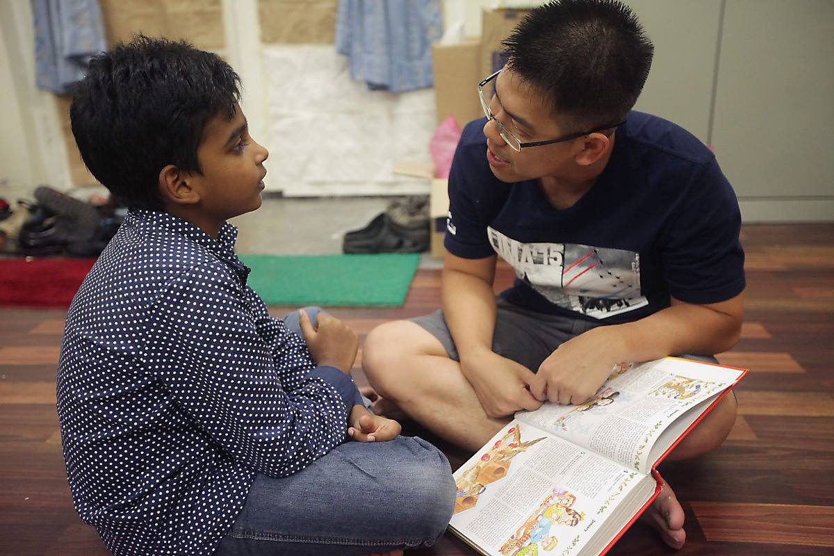 Two children sitting on the floor, looking at an open book together indoors.