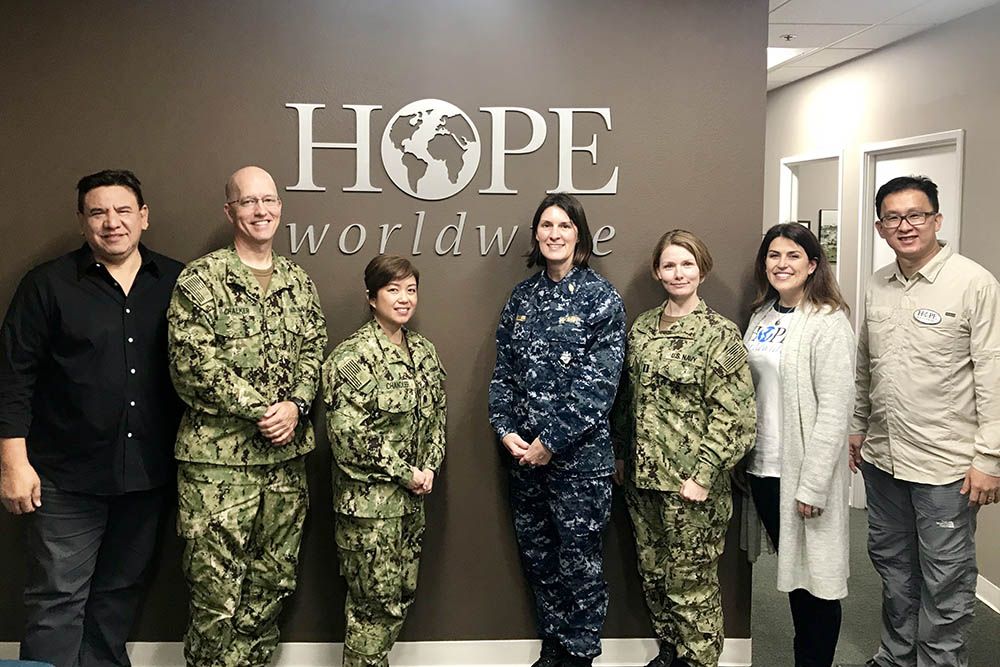 Seven people stand in front of a HOPE Worldwide sign, posing in an office lobby.
