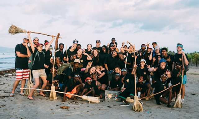 Large group posing on a beach with brooms and tools, celebrating after a cleanup event