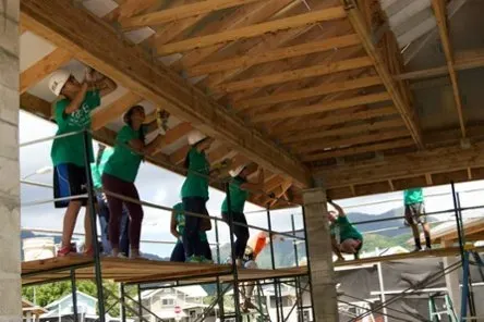 Workers in green shirts installing a wooden roof frame on a scaffolded construction site
