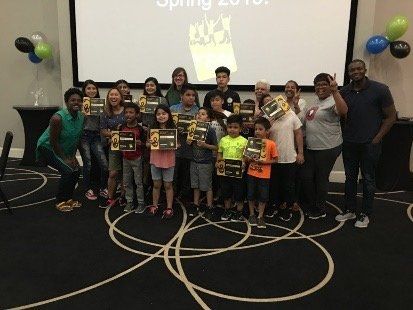 Group of children and adults posing on a stage with trophies and balloons during a spring event