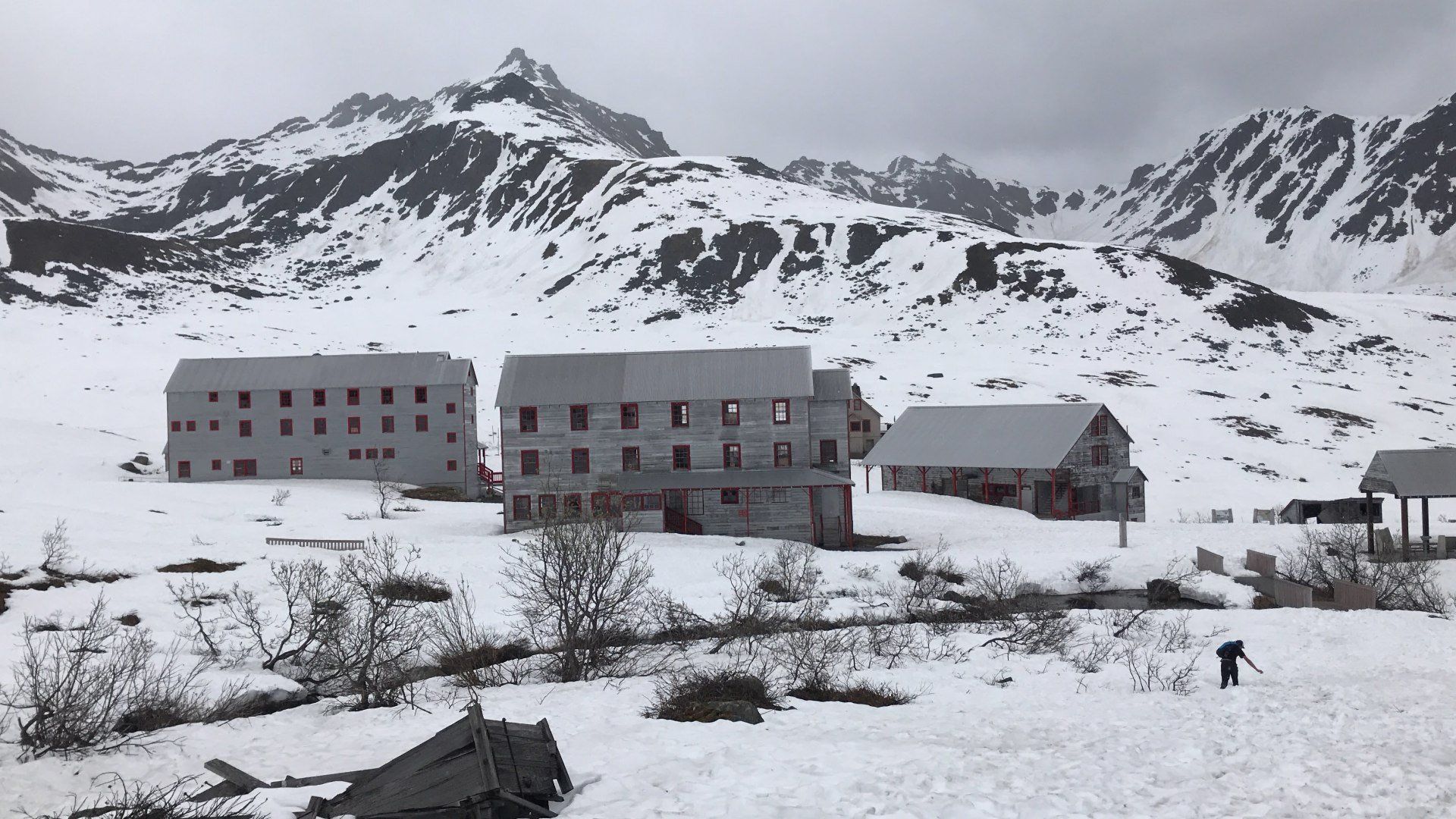 Snow-covered mountain lodge complex with gray buildings and a small person walking in the foreground