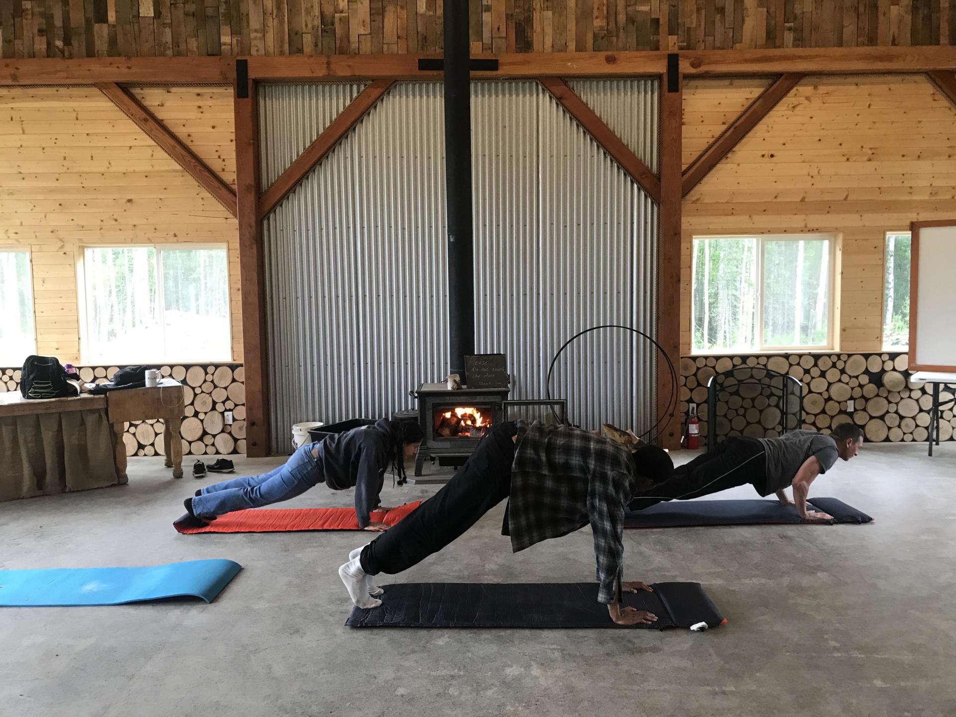 People doing yoga poses in a rustic studio with wood walls and a metal stove