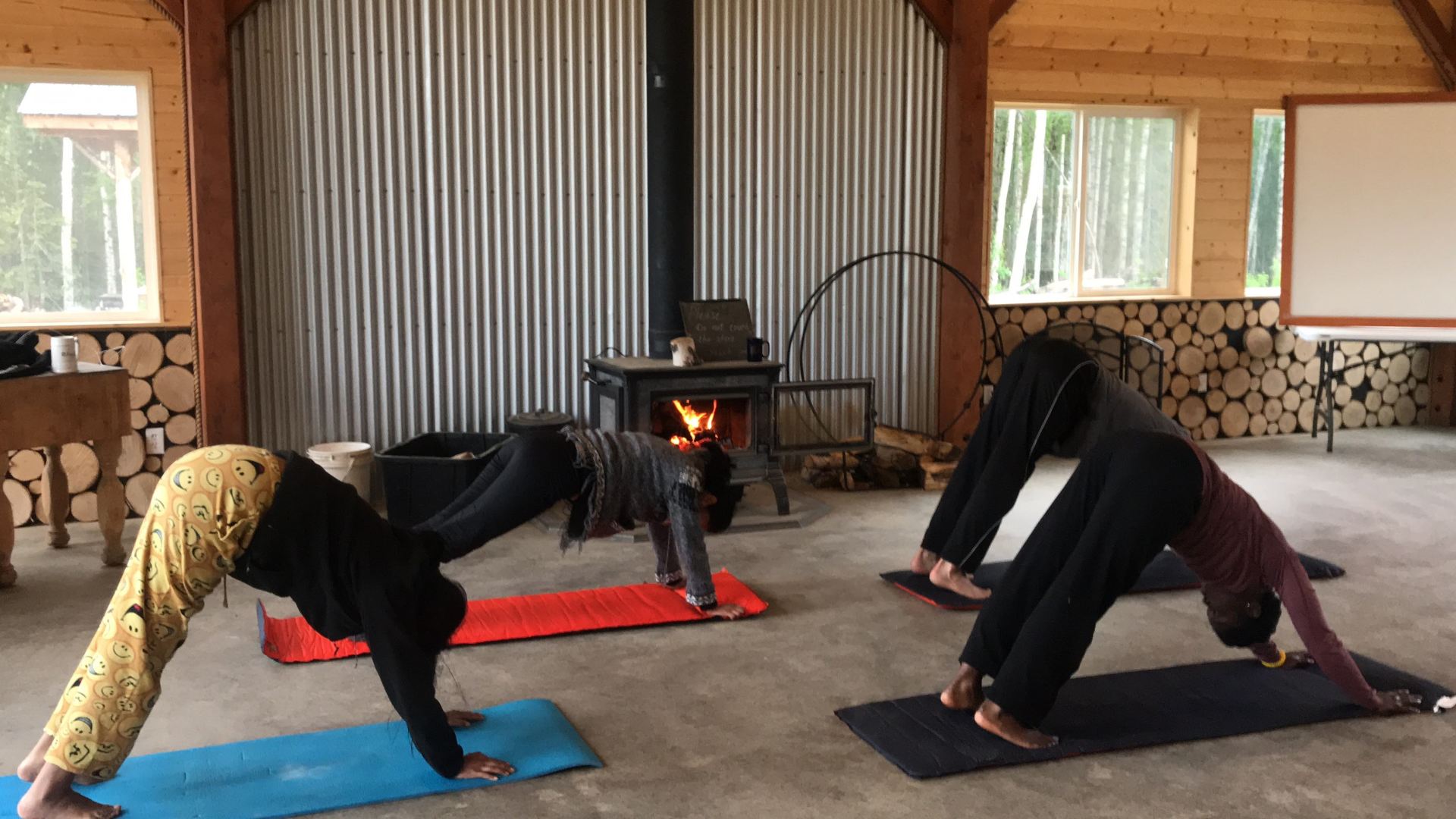 People doing yoga stretches on mats in a rustic room with a wood stove and stone walls