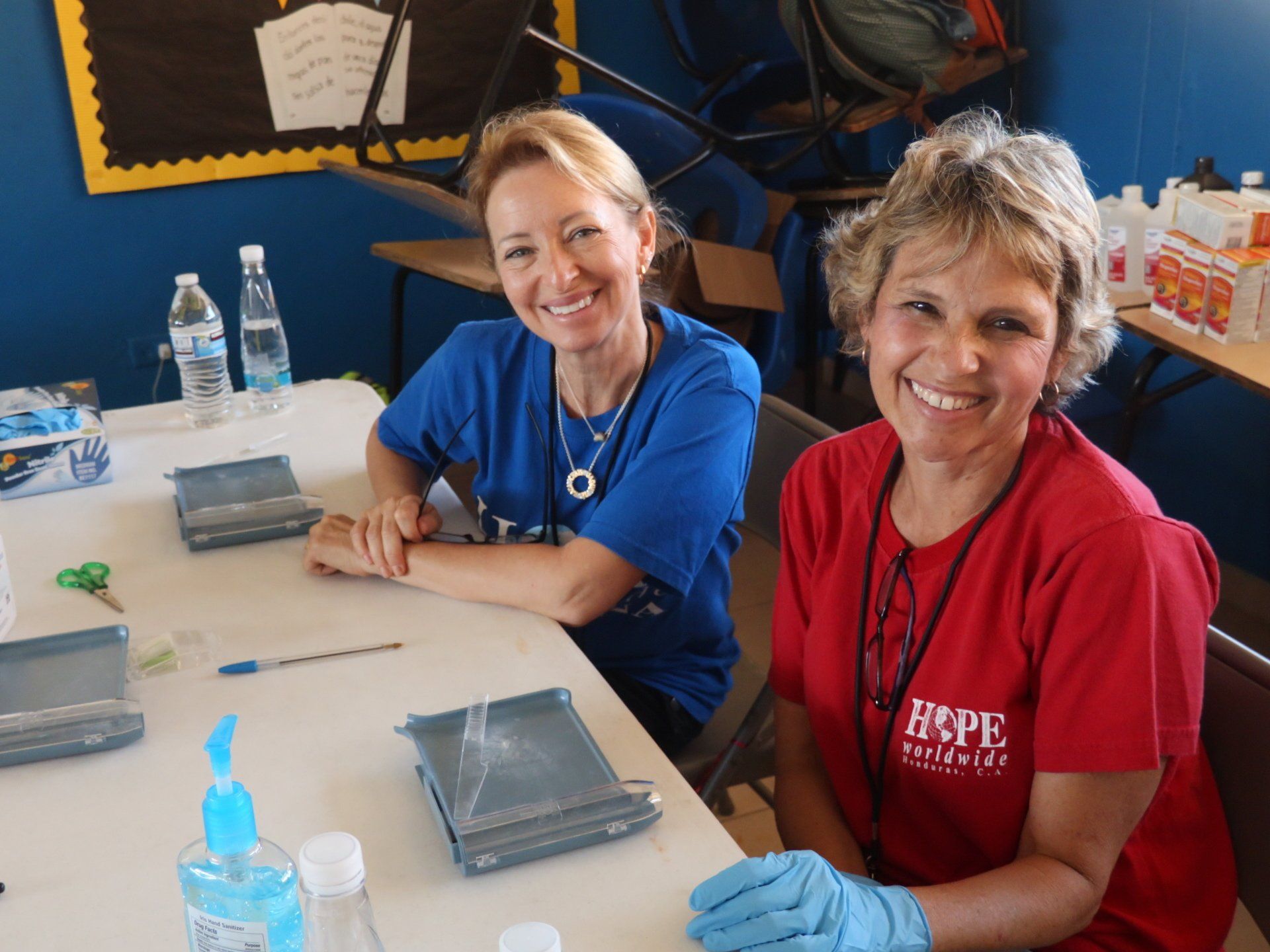 Two smiling people seated at a table with craft supplies in a classroom setting
