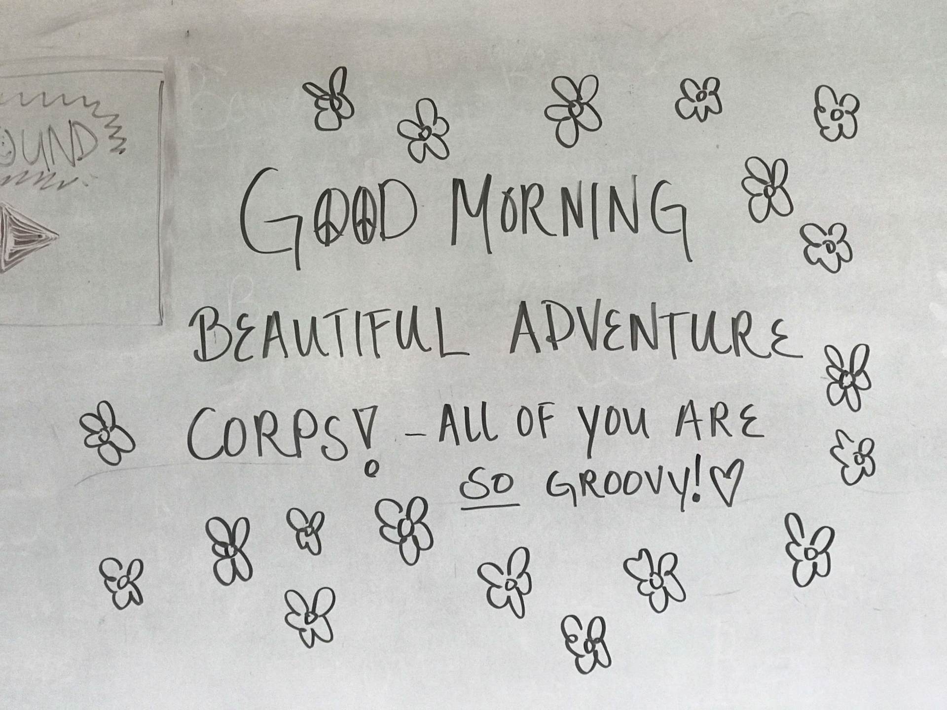 Handwritten message on paper: “Good Morning Beautiful Adventure Corpsy — all of you are so groovy!” with doodled flowers.