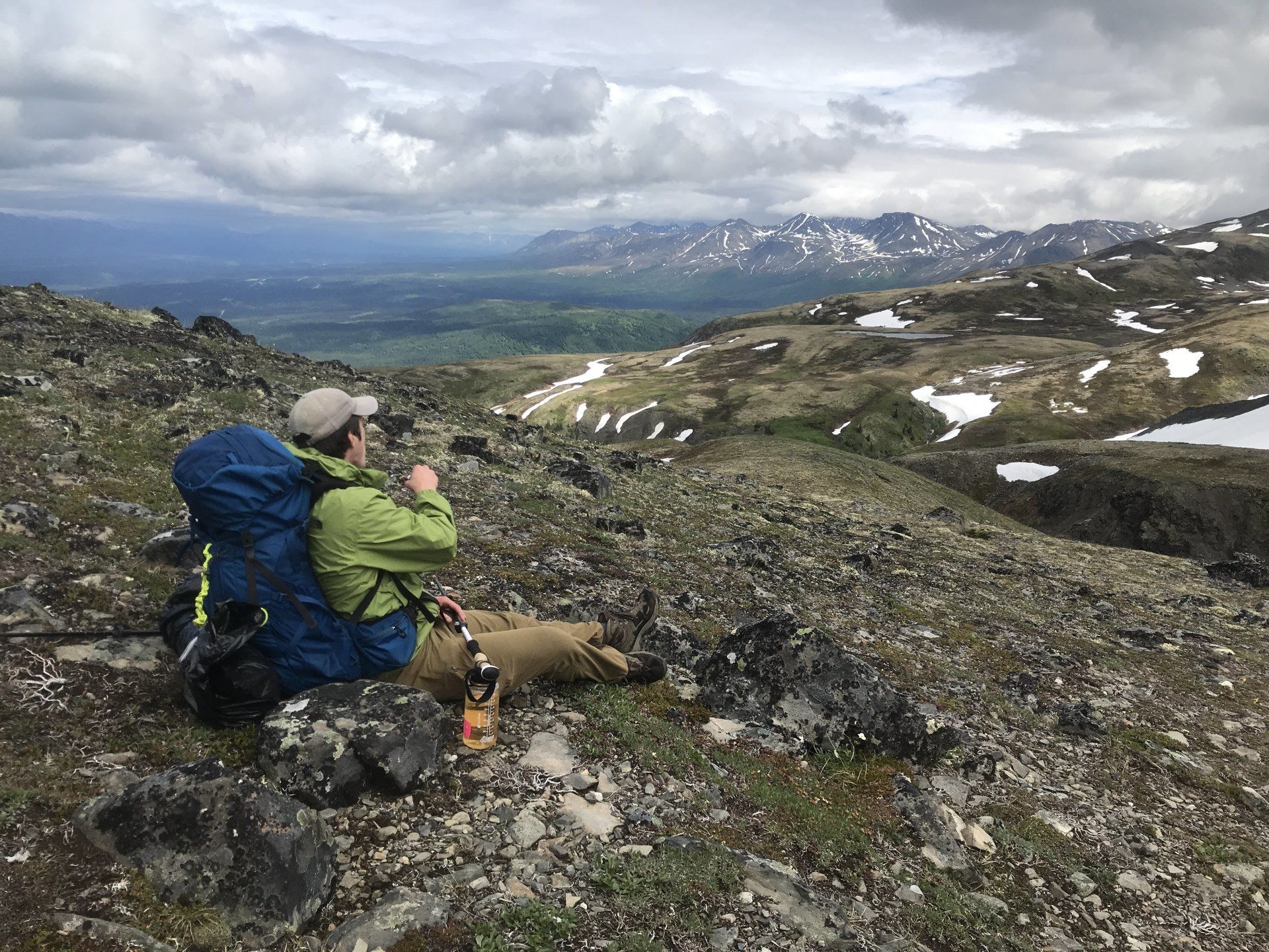 Two hikers rest on a rocky alpine slope overlooking a cloudy mountain valley.