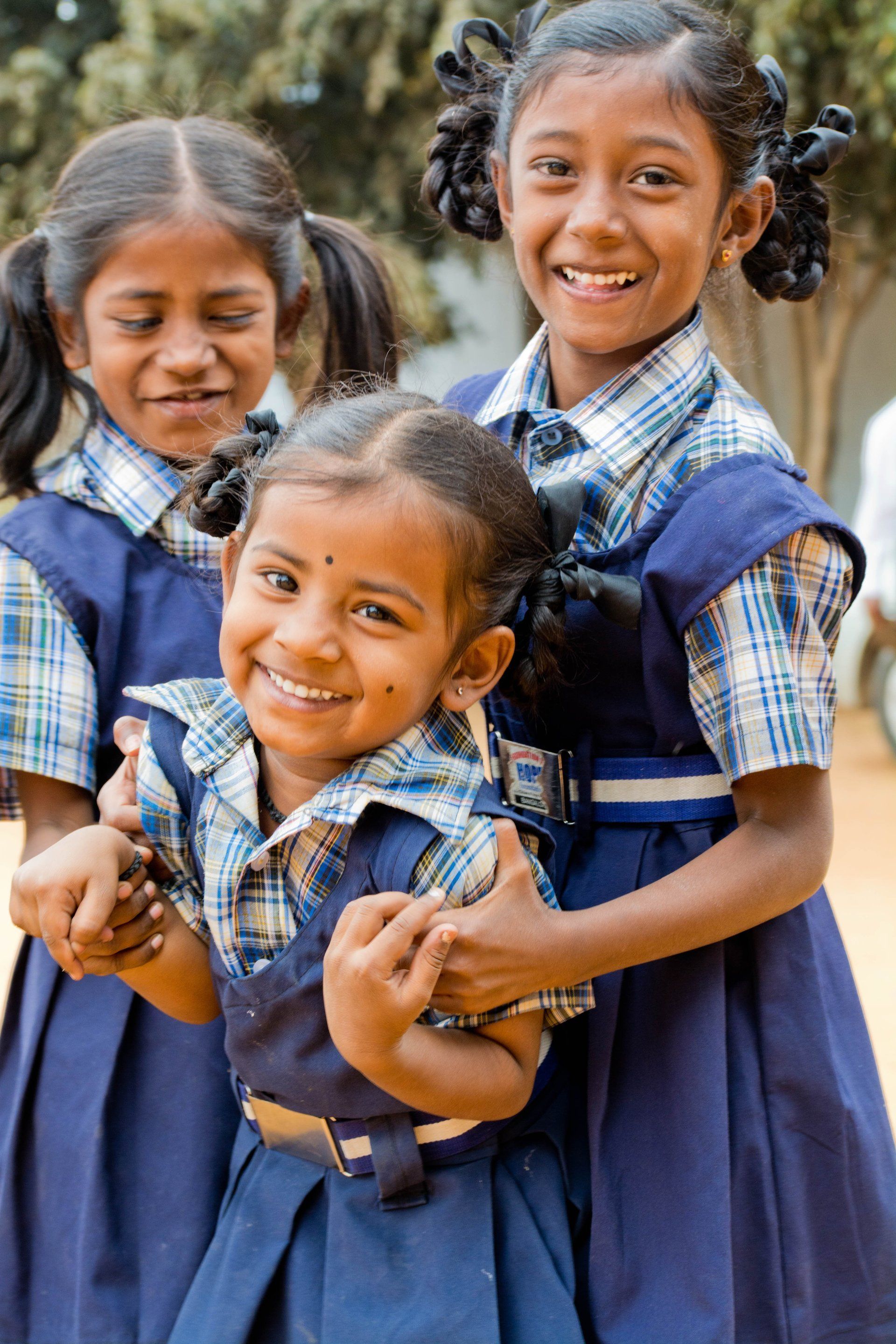 Three smiling schoolchildren in blue uniforms standing close together outdoors