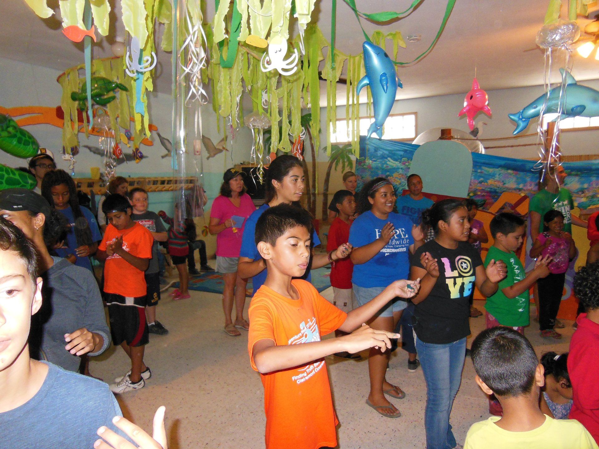 Children dancing at a colorful indoor party with streamers and balloons