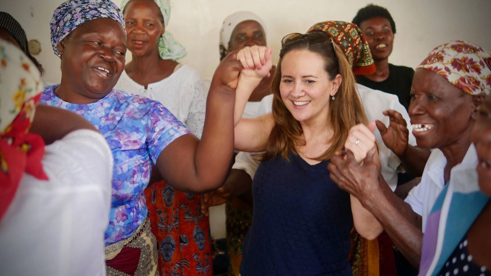 Smiling group raising fists together indoors, celebrating in colorful clothing.
