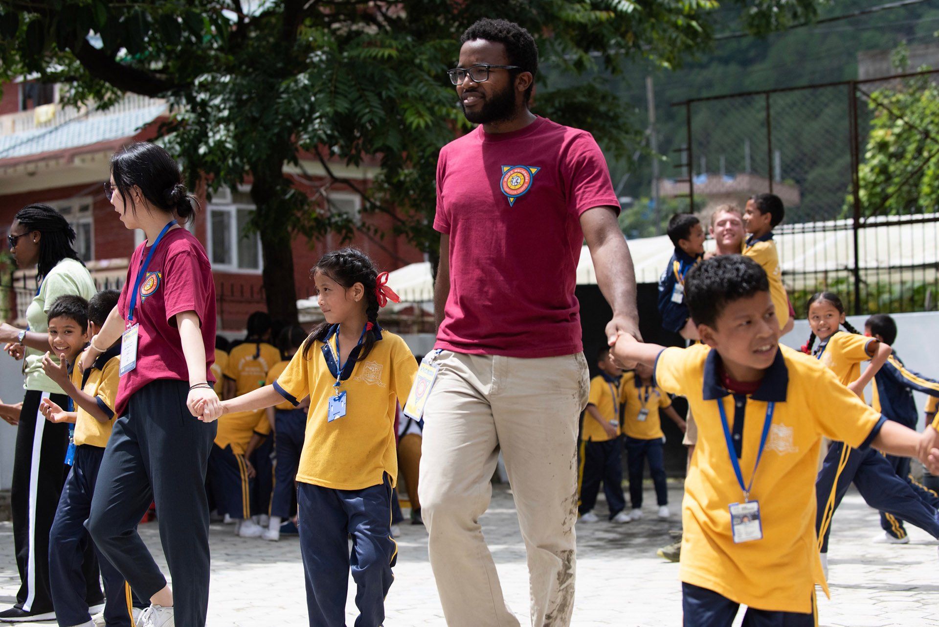 Adult leading children in yellow shirts outdoors, holding hands in a group activity