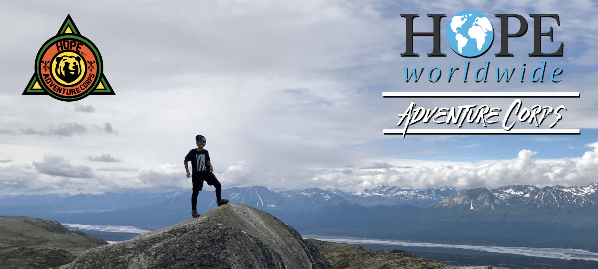Person standing on a mountain peak with “HOPE worldwide” logo and text over a cloudy sky background