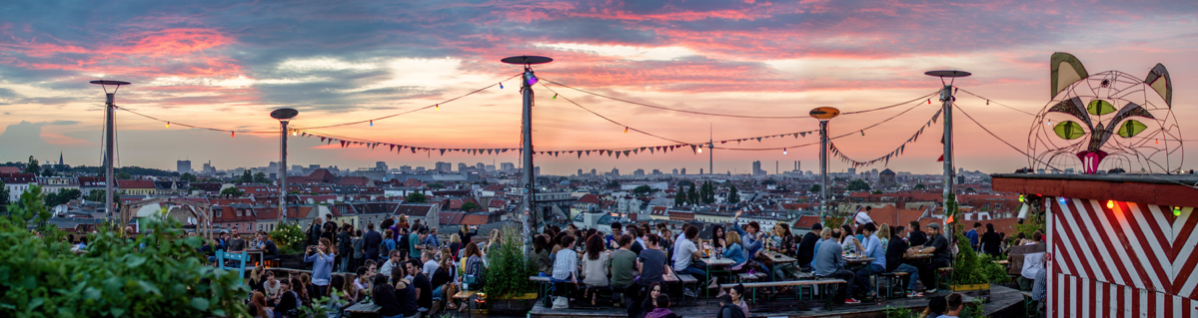 Crowded rooftop concert at sunset with city skyline and pink-orange sky