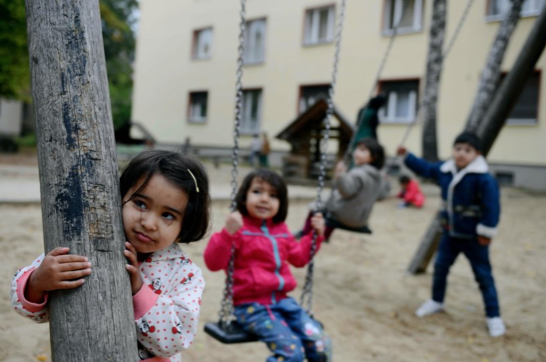 Children playing on swings and climbing in a courtyard playground near an apartment building