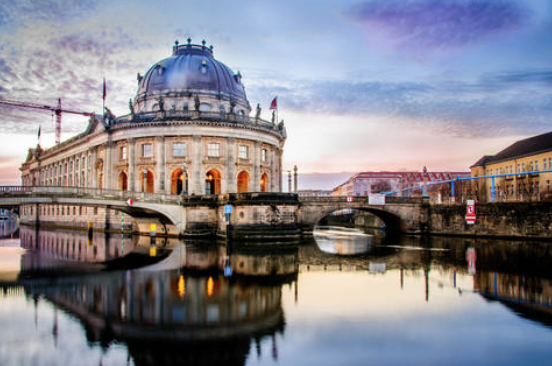 Berlin Cathedral and a bridge over a calm river at sunset, with vivid blue dome reflections in the water