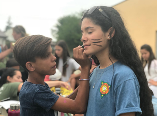 Child face-painting a smiling girl outdoors at a fair