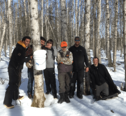 Five people posing in a snowy forest beside a white bucket.