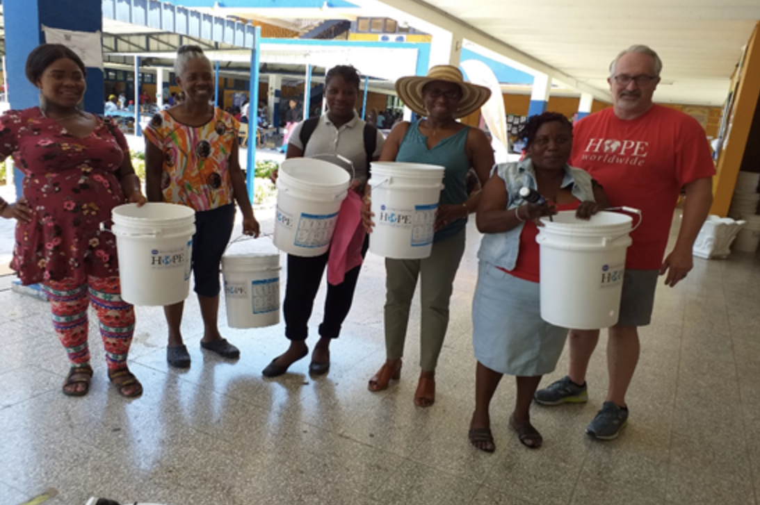 Seven people stand in a school hallway holding white donation buckets.