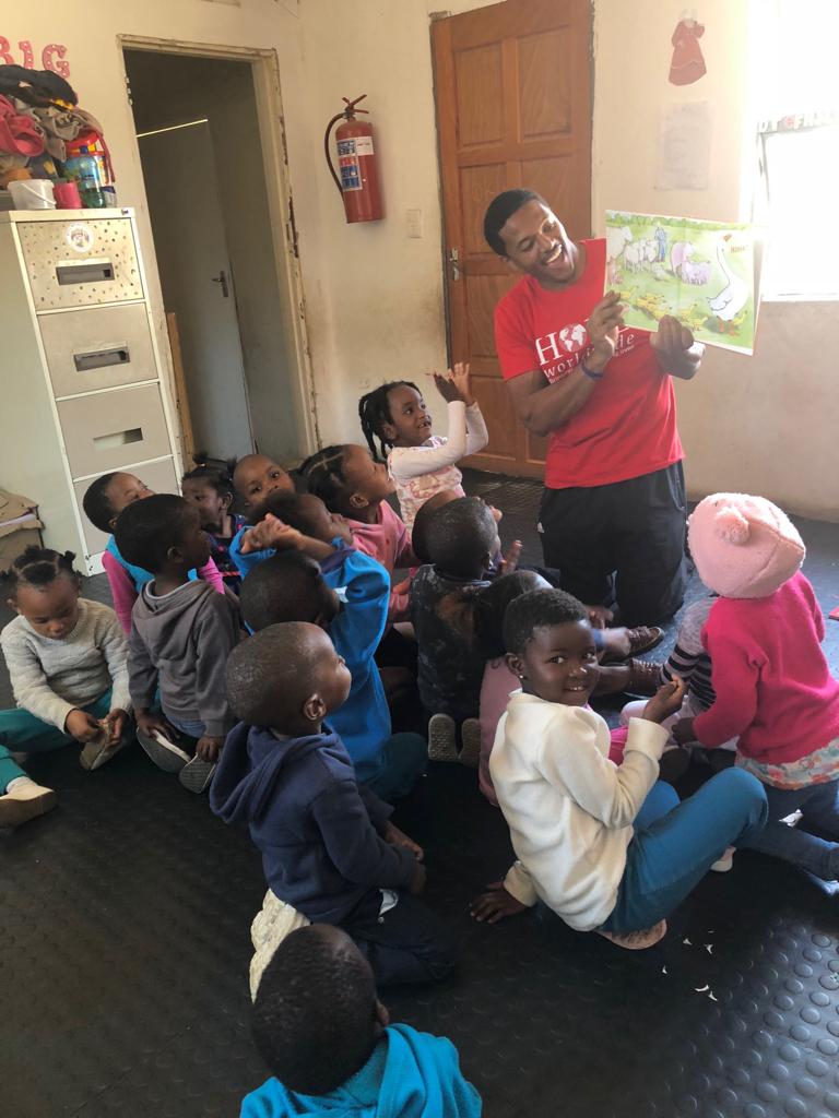 Teacher reading to a seated group of children in a classroom doorway