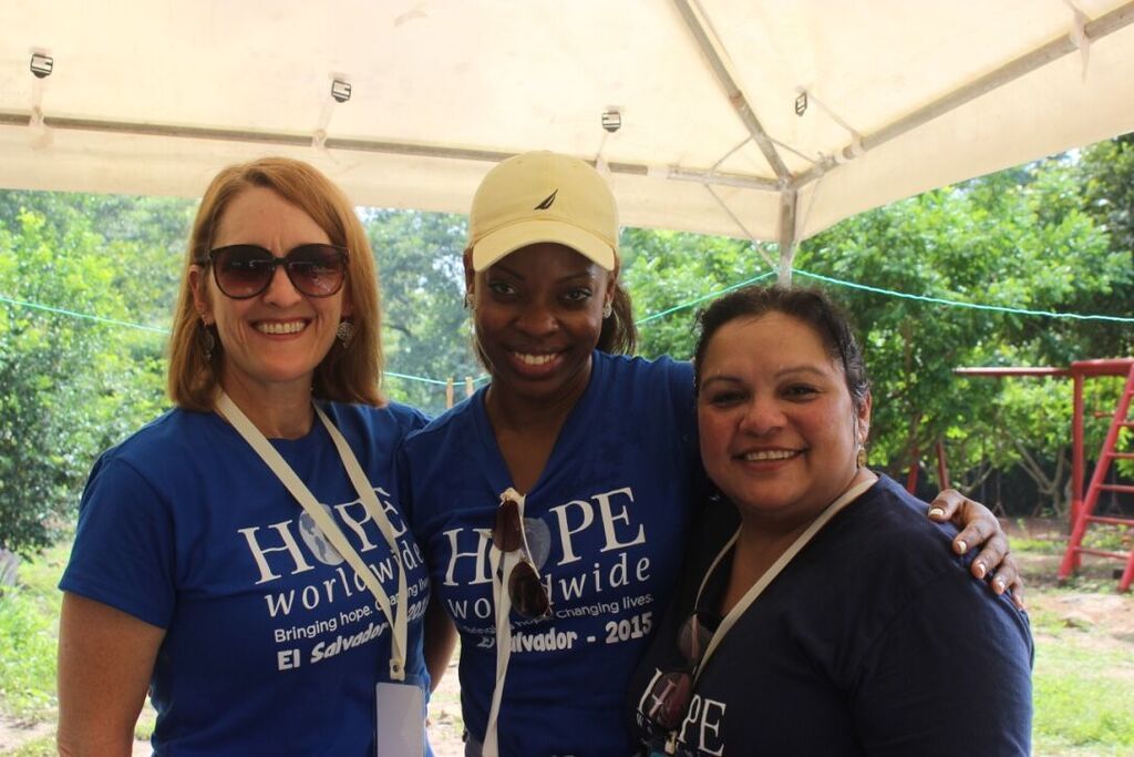 Three smiling people posing under a white tent, wearing blue shirts at an outdoor event.