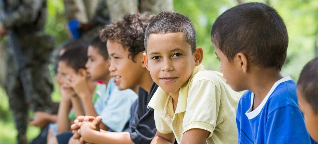 Children sitting outdoors on a bench, one boy in a yellow shirt looking at a boy in blue