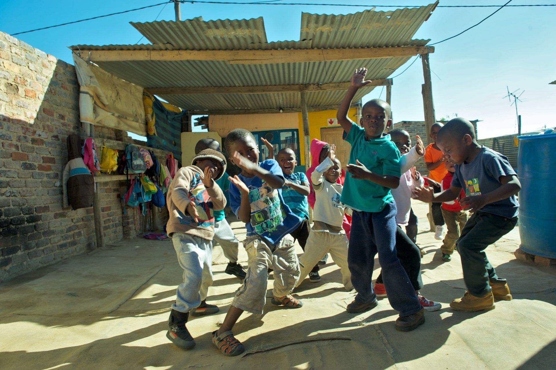Children dancing outdoors in bright clothes beside a corrugated metal building