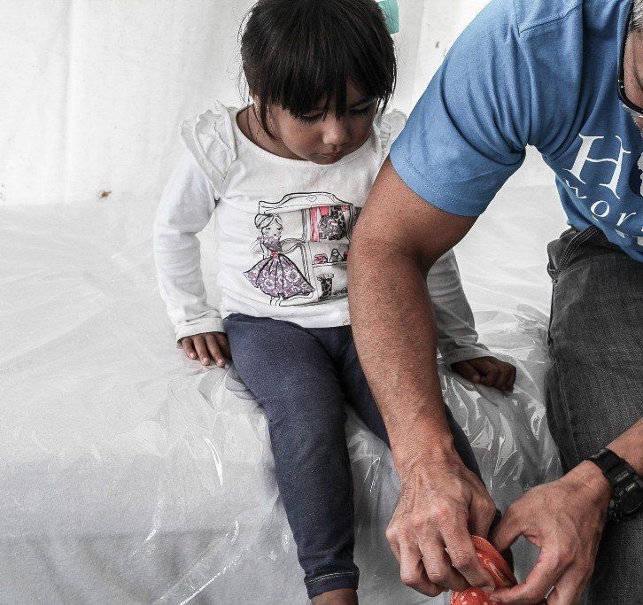 Child sitting on a white sheet while an adult’s hand reaches in from the right.