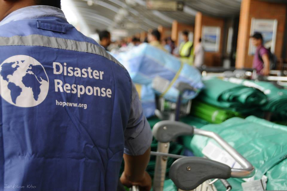 Disaster Response worker in blue vest beside stacked relief supplies indoors