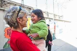 Bolivia-Block.jpg Woman in red shirt smiling while holding a child in a green sweater outdoors.