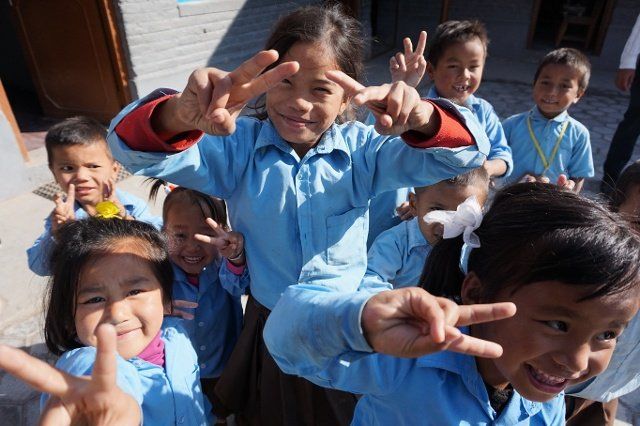 Smiling children in blue shirts pose and flash peace signs outdoors in bright sunlight