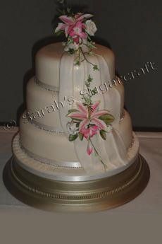 A three tier wedding cake with pink lillies.
