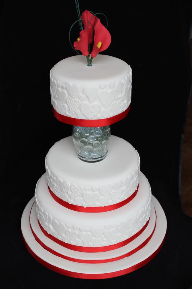 A three-tier white celebration cake with red detailing.