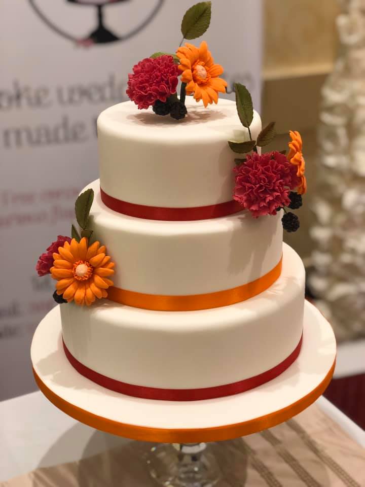 A three tier wedding cake with bright red and orange sugar flowers.
