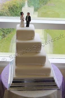 A four-tier side angled wedding cake with two figures on top.