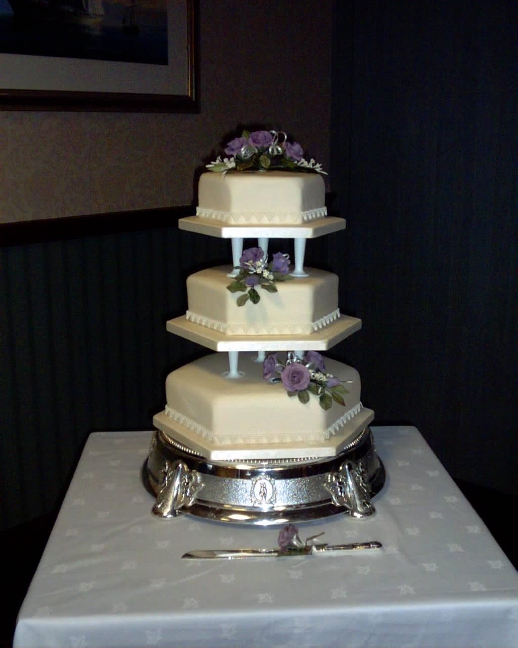 A three tier wedding cake with purple sugar flowers.