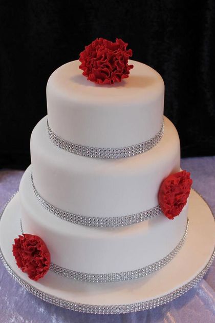 A three-tier white wedding cake with diamante ribbons and 3 red sugar flowers.
