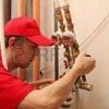 Plumber in red shirt and cap working on pipes, indoors.