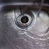 Water flowing into a stainless steel sink, over the drain.