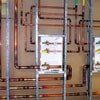 Copper pipes and tubing arranged on a brown wall, with a small display.