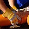 Hands in yellow gloves working on an orange pipe, outdoors.