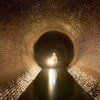 Inside a brick tunnel, light reflects off water, illuminating the dark circular exit.