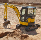 Yellow mini excavator digging in dirt at a construction site.