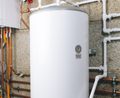 White water heater in a basement with copper and white pipes against a concrete wall.