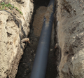 A gray pipe lies in a trench filled with sand, viewed from above.