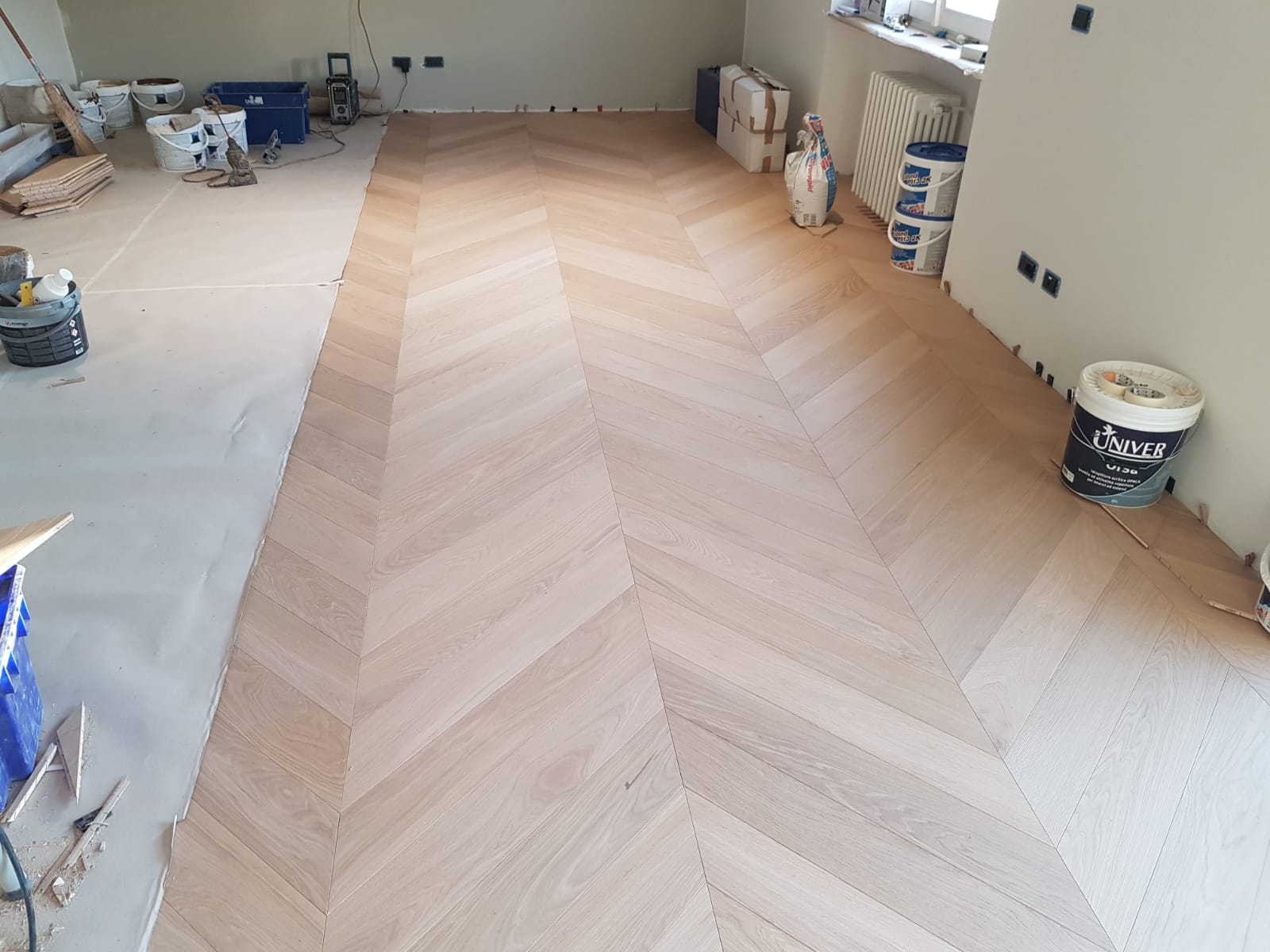 Stanza in ristrutturazione con pavimento in legno chiaro a spina di pesce in fase di installazione
