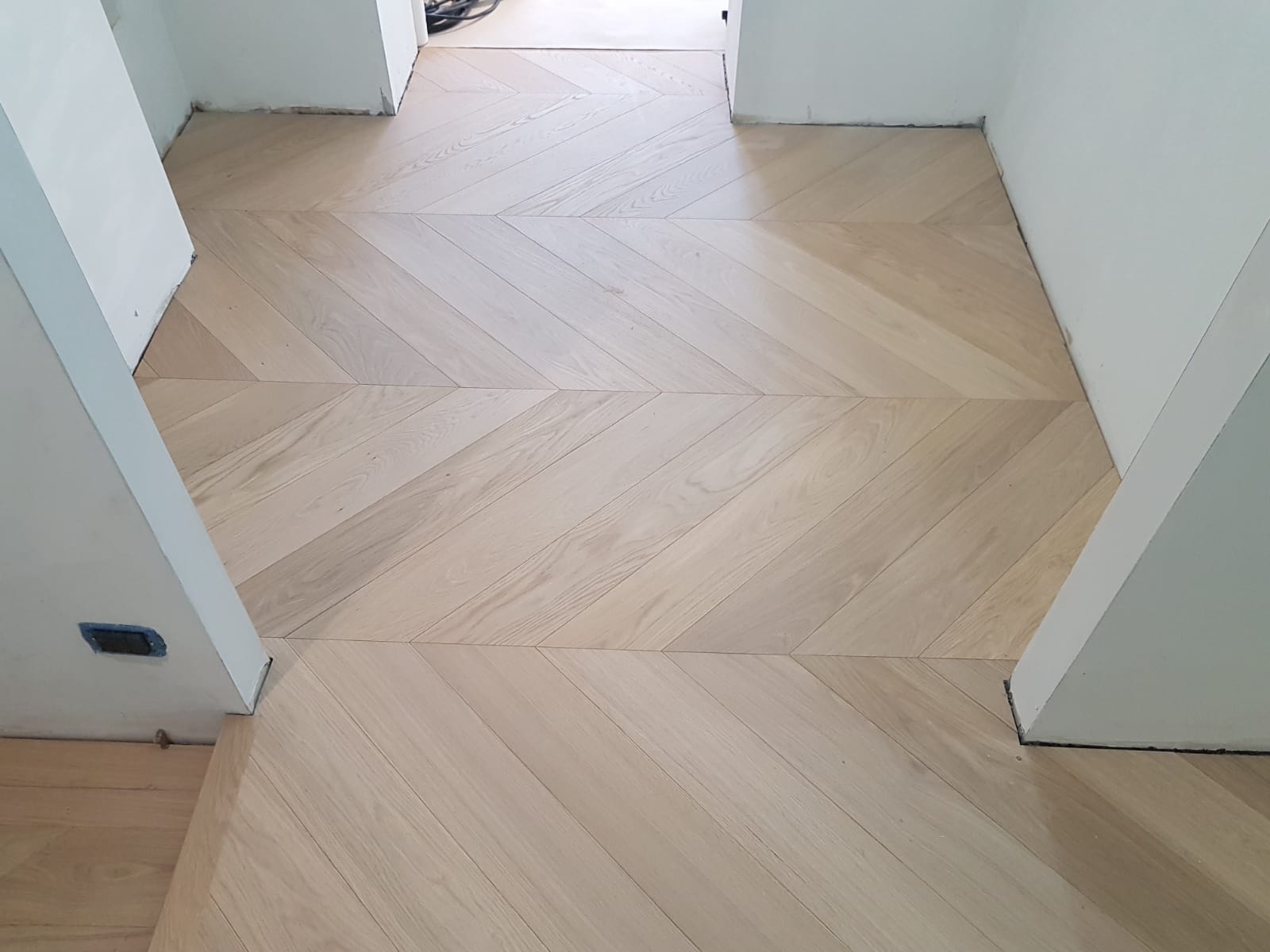Pavimento in legno chiaro a spina di pesce in un corridoio bianco che si apre su una stanza